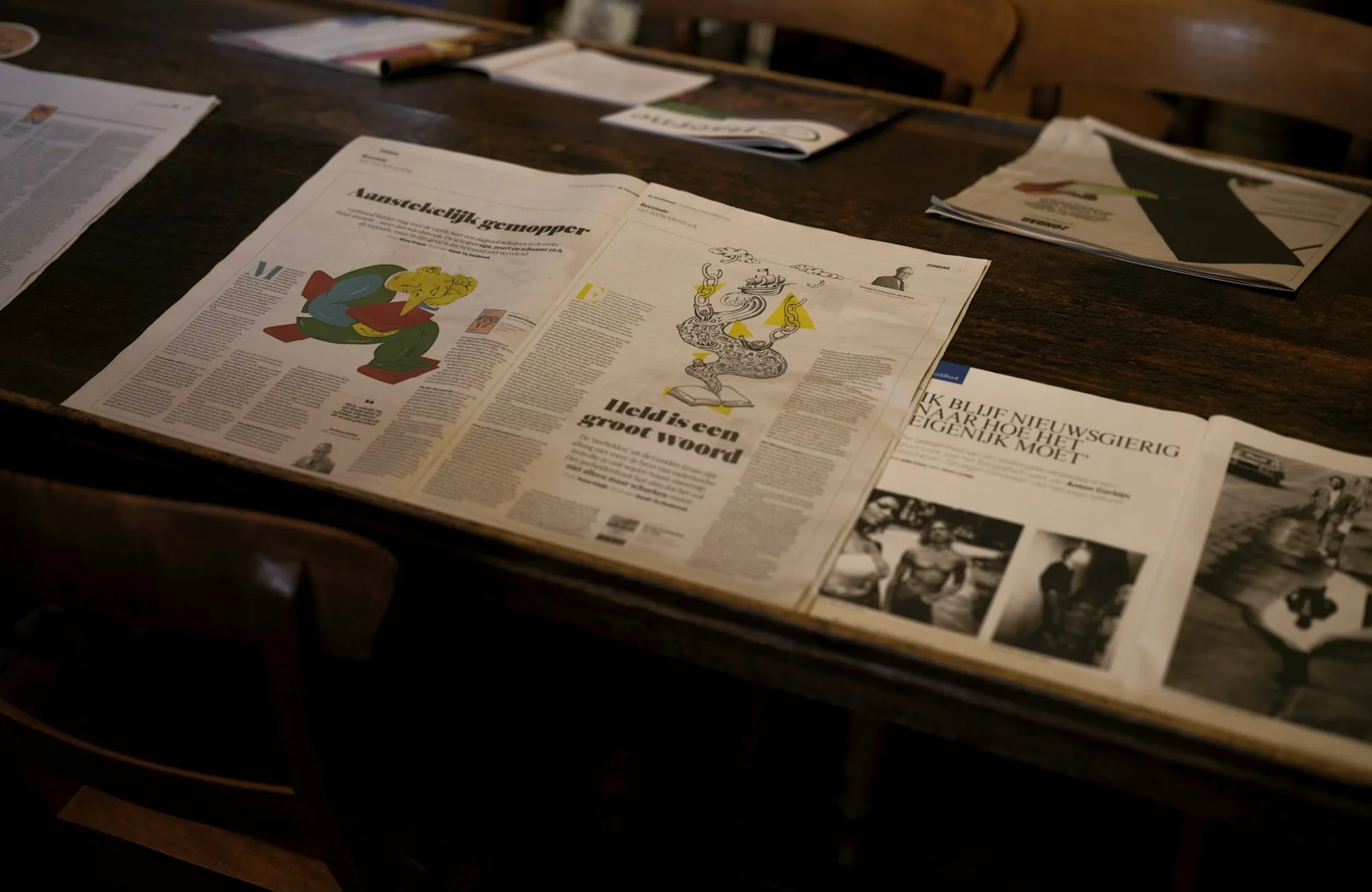 Newspapers and magazines spread across a wooden table in an editorial workspace
